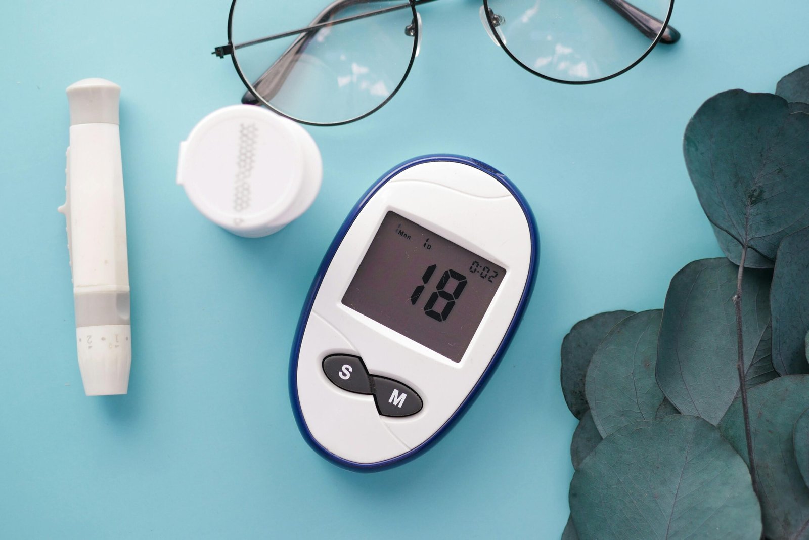 pexels photo 11081349 11081349 A top view of a glucometer, test strip, and glasses on a blue background, symbolizing health management.